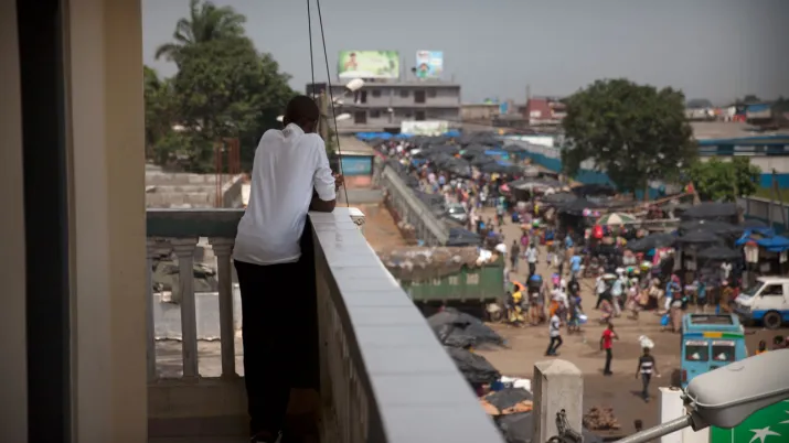 Un jeune homme depuis le balcon regarde la rue animée, Côte d'Ivoire